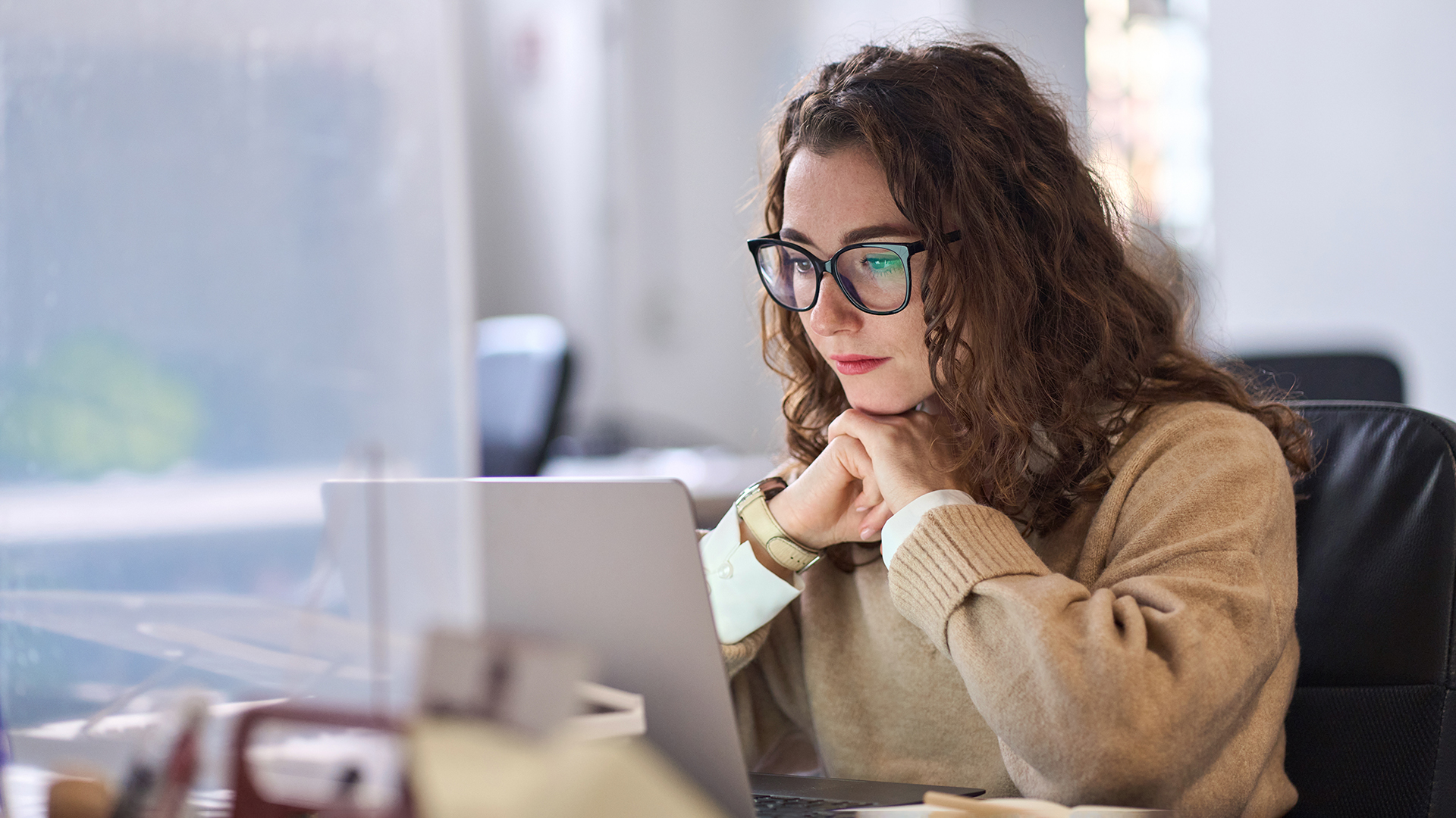 Young professional woman using laptop watching online webinar at work.